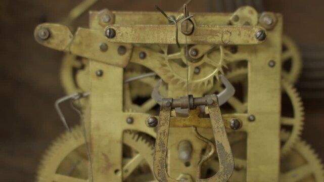 Macro front view shot of a brass mechanical gear ticking and rotating rhythmically inside the internal movement mechanism of a vintage antique grandfather clock.