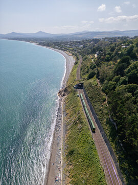 Aerial view of the Dalkey coastal railway line with a train emerging from a tunnel, running along the rocky coastline and the Irish Sea in Dublin, County Dublin, Ireland.