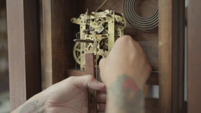 Close up shot of a watchmaker carefully removing the brass mechanical movement and gears from an antique grandfather clock during a restoration process.