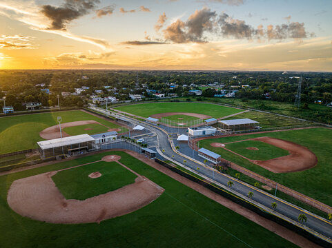 Aerial view of Quality Baseball Academy featuring baseball diamonds, green fields, and palm trees at sunset in San Antonio de Guerra, Santo Domingo Provinc, Dominican Republic.