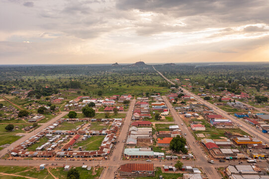 Aerial view of Katakwi Town Council featuring a grid of buildings and market stalls surrounded by lush green plains under a dramatic cloudy sky in Katakwi, Eastern Region, Uganda.