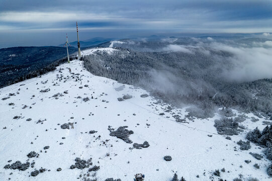 Aerial view of the snowy peak of Hornisgrinde with a communications tower and wind turbine surrounded by winter forest in the Black Forest, Seebach, Baden-Wurttemberg, Germany.