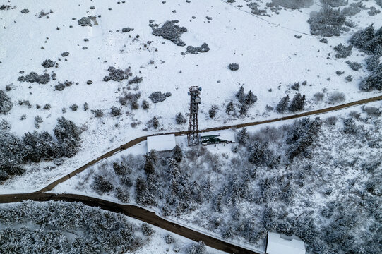Aerial view of a communication tower surrounded by snow-covered pine trees and a winding road near Mummelsee in Seebach, Baden-Wurttemberg, Germany.