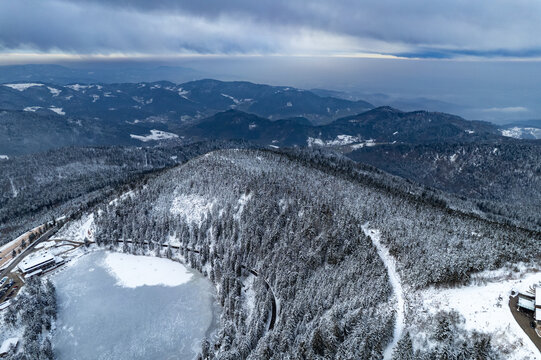 Aerial view of the frozen Mummelsee lake surrounded by snow-covered pine forests and the Black Forest mountains in Seebach, Baden-Wurttemberg, Germany.