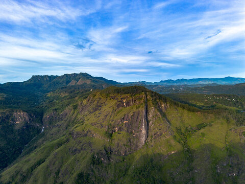 Aerial view of Little Adam's Peak featuring lush green mountain slopes under a bright blue sky with scattered clouds in Badulla, Uva Province, Sri Lanka.