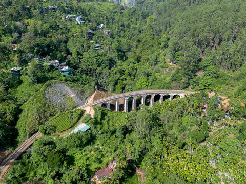 Aerial view of the Nine Arch Bridge surrounded by lush green tea plantations and dense forest in the hills of Demodara, Uva Province, Sri Lanka.