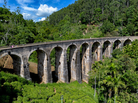 Aerial view of the historic Nine Arch Bridge surrounded by lush green tea plantations and dense forest in Demodara, Uva Province, Sri Lanka.