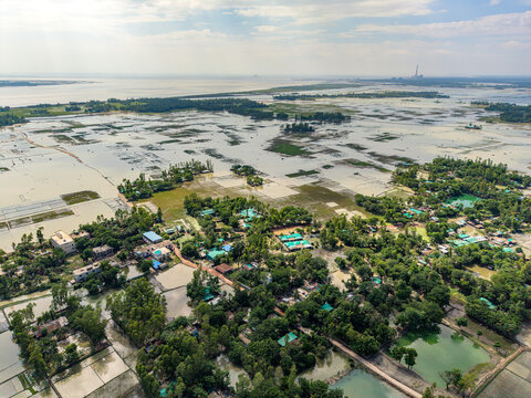 Aerial view of the flooded rural landscape with scattered houses, lush green trees, and water-covered agricultural fields in Banshkhali Upazila, Chittagong Division, Bangladesh.