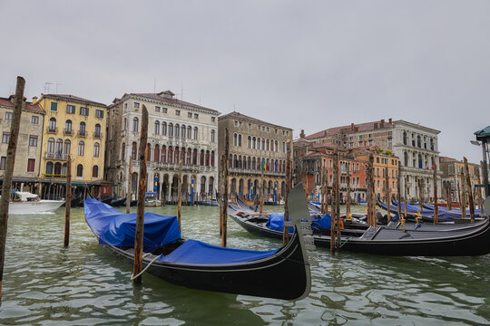 Venice, Italy - 06 May 2022: View of gondolas moored on the Grand Canal with historic Venetian buildings in the background under a cloudy sky.