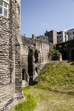 View of the historic stone walls and fortifications of Newcastle Castle with grassy embankments and modern buildings in the background in Newcastle upon Tyne, England, United Kingdom.