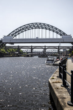 View of the iconic Tyne Bridge spanning the River Tyne with other historic bridges in the background, seen from the paved waterfront in Newcastle upon Tyne, England, United Kingdom.