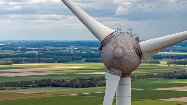 Aerial view of a wind turbine hub and blades set against a backdrop of green and brown agricultural fields in the flat landscape of the Flevoland province, Rutten, Flevoland, Netherlands.