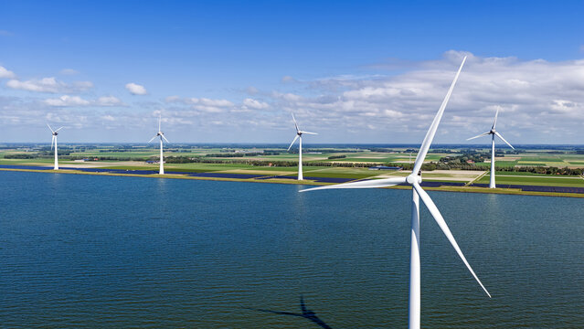 Aerial view of wind turbines standing in the water along the green coastline of Rutten, Flevoland, Netherlands.