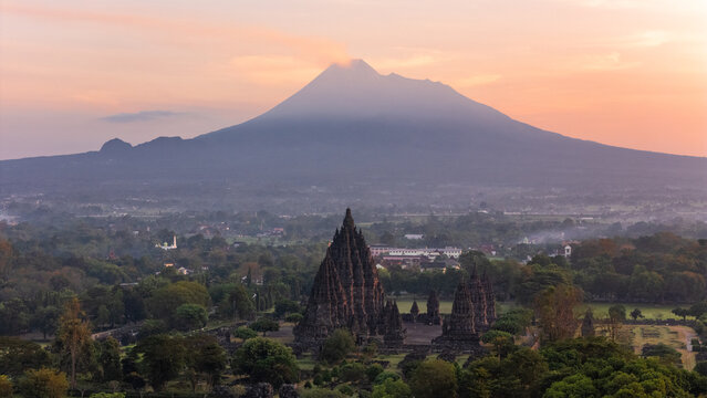 Aerial view of Prambanan Temple with Mount Merapi volcano in the background at sunrise, surrounded by lush greenery in Kecamatan Prambanan, Daerah Istimewa Yogya, Indonesia.