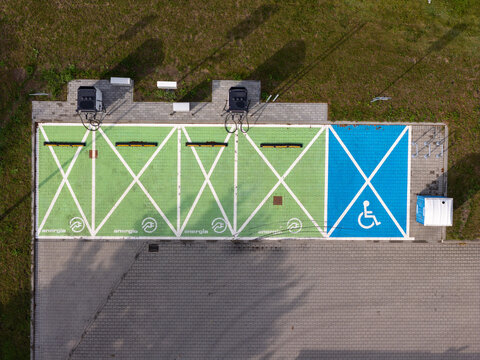 Aerial view of an electric vehicle charging station featuring green parking spaces with charging symbols and a blue accessible parking spot in Gdansk, Pomeranian Voivodeship, Poland.