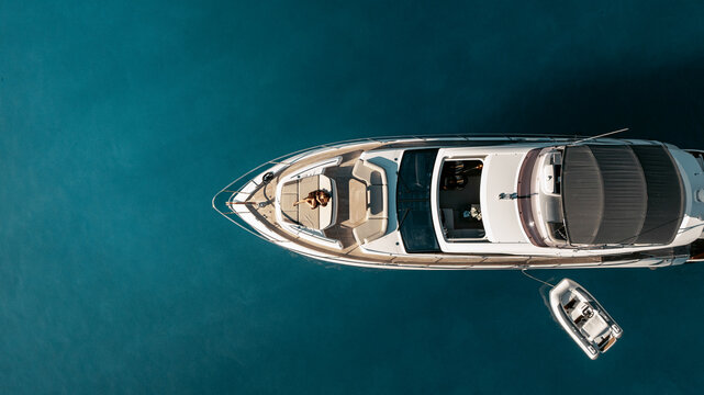 Balearic Islands, Spain - 20 April 2024: Aerial view of a luxury yacht anchored in the turquoise waters of Mallorca with a person relaxing on the deck and a small tender boat nearby.