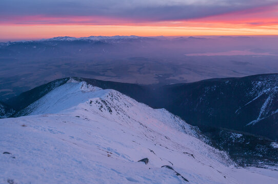 View of the snow-covered peak of Baranec in the Western Tatras during a vibrant sunset with purple and orange skies over the mountain range in Jamnik, Zilina Region, Slovakia.