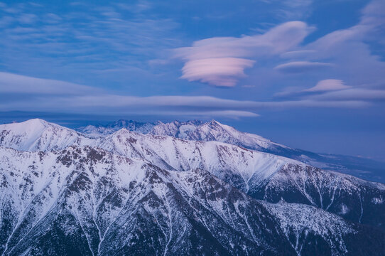 Aerial view of the snow-capped peaks of the High Tatras mountains under a sky filled with unique lenticular clouds in Vysoke Tatry, Presov Region, Slovakia.