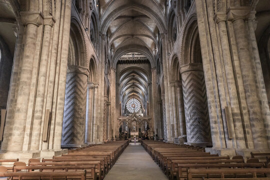 View of the interior of Durham Cathedral, featuring massive Norman columns with chevron carvings, a long nave with wooden pews, and a rose window in Durham, England, United Kingdom.