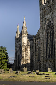 View of the historic Durham Cathedral with its gothic spires and stone architecture rising above a peaceful graveyard with ancient headstones and green grass in Durham, England, United Kingdom.