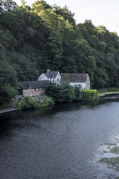 View of a historic stone building nestled along the riverbank surrounded by dense woodland in Durham, England, United Kingdom.