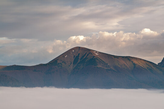 Aerial view of Stoh mountain in Mala Fatra rising above a thick layer of clouds with soft golden light on the peak in Turany, Zilina Region, Slovakia.