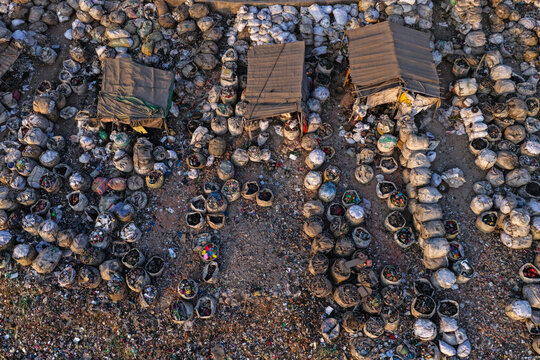 Aerial view of numerous sacks filled with plastic waste and recycling materials arranged in rows with makeshift shelters near the Buriganga River in Dhaka, Dhaka Division, Bangladesh.