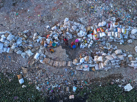 Aerial view of people sorting through piles of waste and recyclables in sacks along the Buriganga Riverbank in Dhaka, Dhaka Division, Bangladesh.