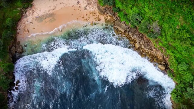 Aerial view of waves crashing against the rocky coastline and sandy shore at Timang Beach in Kecamatan Tepus, Daerah Istimewa Yogya, Indonesia.