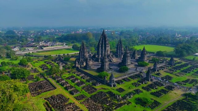 Aerial view of the historic Prambanan Temple complex with its stone spires surrounded by lush green lawns and ancient ruins in Kecamatan Prambanan, Daerah Istimewa Yogya, Indonesia.