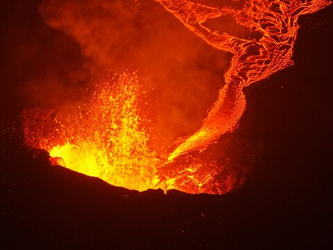Aerial view of a powerful volcanic eruption with glowing lava flows and thick smoke rising into the night sky in Reykjavik, Reykjavikurborg, Iceland.