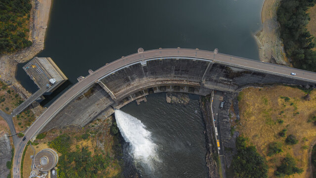 Aerial view of the Barrage de Villerest showing the curved concrete dam structure with water discharging into the river in Commelle-Vernay, Auvergne-Rhone-Alpes, France.