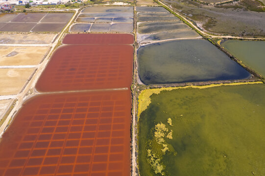 Aerial view of the Salinas do Grelha salt pans featuring vibrant red and green water basins separated by earthen paths in Olhao, Faro, Portugal.