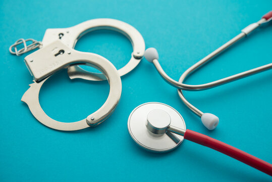 Handcuffs and stethoscope on blue background. Medical crime, services without a license, malpractice and so on. Medical law rules regulations in the health care industry and its patients concept.