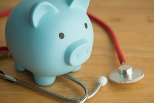 Blue piggy bank and red stethoscope on wooden table background copy space. Money savings for medical, healthcare, life insurance or personal financial checkup and so on concept.
