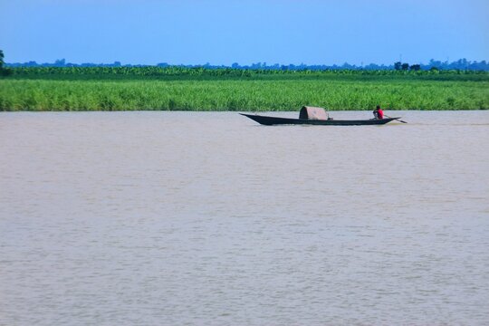 View of a lone fisherman rowing a small wooden boat on the calm waters of the river with lush green fields in the background in Kushtia, Khulna Division, Bangladesh.