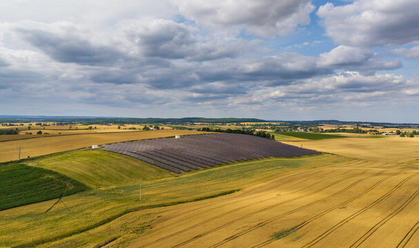 Aerial view of a solar farm situated in the middle of golden agricultural fields under a cloudy sky in Tczew, Pomeranian Voivodeship, Poland.