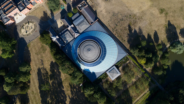 Aerial view of Wellcome Genome Campus featuring a distinctive circular glass dome roof surrounded by landscaped grounds and trees in Hinxton, England, United Kingdom.