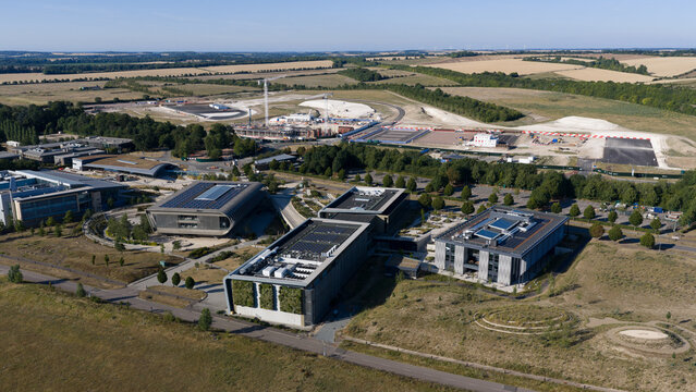 Aerial view of the Wellcome Genome Campus featuring modern research buildings with green roofs and solar panels, surrounded by landscaped grounds in Hinxton, England, United Kingdom.