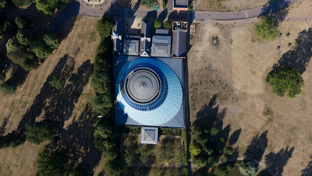 Aerial view of the Wellcome Genome Campus featuring its distinctive circular glass roof surrounded by lush parkland and trees in Hinxton, England, United Kingdom.