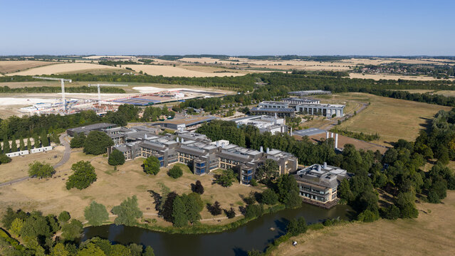 Aerial view of the Wellcome Genome Campus featuring modern research buildings, surrounding parkland, and a small lake in Hinxton, England, United Kingdom.