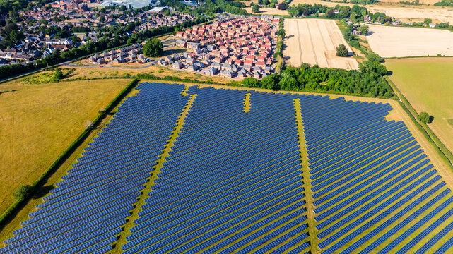 Aerial view of a large solar farm with rows of photovoltaic panels situated next to a residential neighborhood and agricultural fields in Dorset, England, United Kingdom.