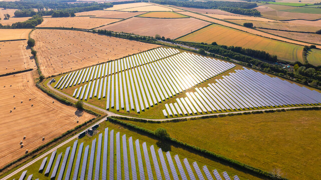 Aerial view of a solar farm with rows of photovoltaic panels situated in agricultural fields with hay bales and green pastures in the countryside in Dorset, England, United Kingdom.