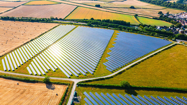 Aerial view of a large solar farm with rows of photovoltaic panels set in a rural landscape surrounded by agricultural fields and hedgerows in Dorset, England, United Kingdom.