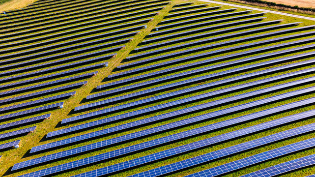 Aerial view of a large solar farm with rows of photovoltaic panels arranged in neat lines across a grassy field in Dorset, England, United Kingdom.