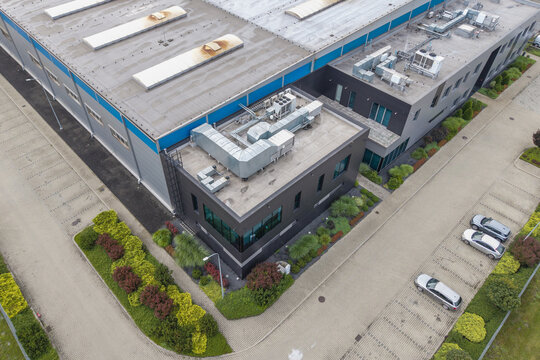 Aerial view of a modern logistics hub with industrial warehouse buildings, rooftop ventilation, paved parking with cars, and landscaped greenery in Skawina, Lesser Poland Voivode, Poland.