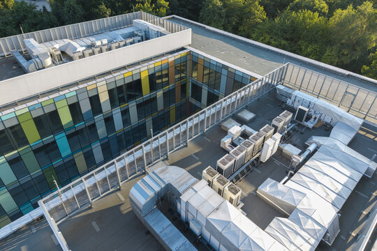 Aerial view of the AI data center cooling system featuring rows of HVAC units and metal ductwork on a modern rooftop with a colorful glass facade in Krakow, Lesser Poland Voivode, Poland.
