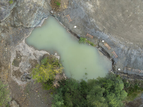 Aerial view of the porphyry and diabase mine featuring a turquoise water pond, rocky quarry walls, surrounding trees, and industrial equipment in Krakow, Lesser Poland Voivode, Poland.