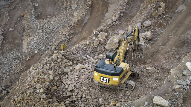 Aerial view of a yellow Caterpillar excavator working in the kopalnia porfiru i diabazu quarry surrounded by rocky terrain and dirt paths in Krakow, Lesser Poland Voivode, Poland.