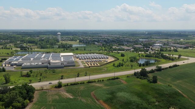 Aerial view of a modern data center facility with rooftop solar panels surrounded by green fields and rural landscape in Volo, Illinois, United States.